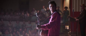 Movie still from “Elvis” (2022), directed by Baz Luhrmann – A man holding a microphone while standing in front of an audience; Medium shot, Over the shoulder angle