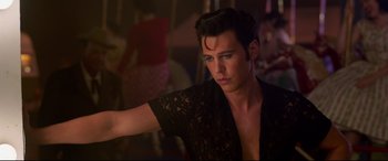 Movie still from “Elvis” (2022), directed by Baz Luhrmann – A man in a black shirt is posing for a picture; Medium shot, Over the shoulder angle