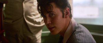 Movie still from “Elvis” (2022), directed by Baz Luhrmann – A young man in a suit and tie looking at the camera; Close Up shot, Over the shoulder angle