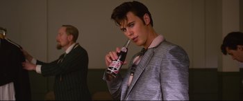 Movie still from “Elvis” (2022), directed by Baz Luhrmann – A man in a suit and tie holding a bottle of soda; Medium shot, Low angle