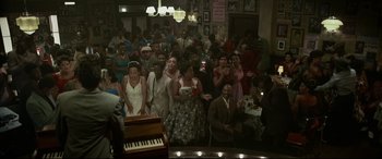 Movie still from “Elvis” (2022), directed by Baz Luhrmann – A group of people standing in a room with a piano in front of them; Wide shot, High angle