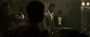 Movie still from “Elvis” (2022), directed by Baz Luhrmann – A man standing in front of a microphone in front of another man; Medium shot, Over the shoulder angle