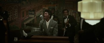 Movie still from “Elvis” (2022), directed by Baz Luhrmann – A man singing into a microphone in front of two other men in suits; Medium shot, Low angle