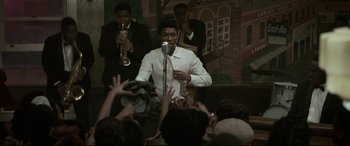 Movie still from “Elvis” (2022), directed by Baz Luhrmann – A group of people are gathered around a microphone; Medium shot, High angle