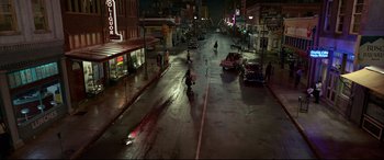 Movie still from “Elvis” (2022), directed by Baz Luhrmann – A city street at night with people on the sidewalk and cars on the street; Extreme Wide shot, High angle