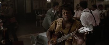 Movie still from “Elvis” (2022), directed by Baz Luhrmann – A woman playing an instrument in front of other people; Medium shot, Over the shoulder angle