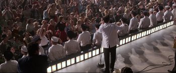 Movie still from “Elvis” (2022), directed by Baz Luhrmann – A man in a white jacket is holding a microphone; Wide shot, High angle