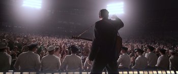 Movie still from “Elvis” (2022), directed by Baz Luhrmann – A man holding a guitar in front of an audience; Wide shot, High angle