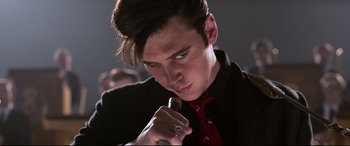Movie still from “Elvis” (2022), directed by Baz Luhrmann – A man in a black suit and a red neck tie; Close Up shot, Low angle