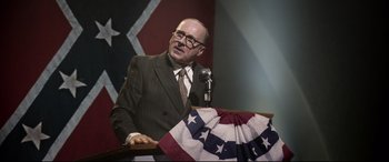 Movie still from “Elvis” (2022), directed by Baz Luhrmann – A man in a suit and glasses speaking at a podium; Medium shot, Over the shoulder angle