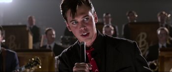 Movie still from “Elvis” (2022), directed by Baz Luhrmann – A man in a suit and tie holding a microphone in his hand; Close Up shot, Over the shoulder angle