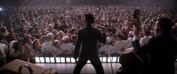 Movie still from “Elvis” (2022), directed by Baz Luhrmann – A crowd of people watching a man on a stage sing; Wide shot, High angle