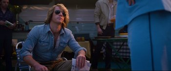 Movie still from “Elvis” (2022), directed by Baz Luhrmann – A man sitting on the ground holding papers; Medium shot, Low angle