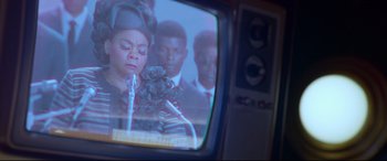 Movie still from “Elvis” (2022), directed by Baz Luhrmann – A television screen showing a man and two women in suits; Extreme Close Up shot, Over the shoulder angle