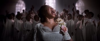 Movie still from “Elvis” (2022), directed by Baz Luhrmann – A woman in a white dress singing in front of a group of people; Medium shot, Low angle