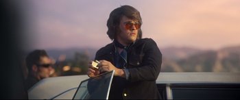 Movie still from “Elvis” (2022), directed by Baz Luhrmann – A man in sunglasses and a jacket holding a cell phone; Medium shot, Low angle