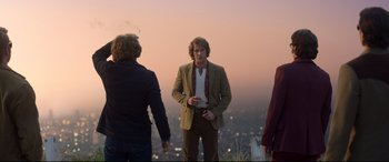 Movie still from “Elvis” (2022), directed by Baz Luhrmann – A man smoking a cigarette while standing next to two other men; Medium shot, Over the shoulder angle