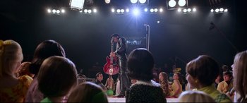 Movie still from “Elvis” (2022), directed by Baz Luhrmann – A man in a leather jacket holding a red guitar; Wide shot, Low angle