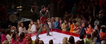 Movie still from “Elvis” (2022), directed by Baz Luhrmann – A man holding a guitar on a stage with a crowd of onlookers; Wide shot, High angle