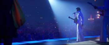Movie still from “Elvis” (2022), directed by Baz Luhrmann – A man standing on a stage holding a microphone; Wide shot, Low angle