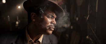 Movie still from “Elvis” (2022), directed by Baz Luhrmann – A man in a hat smoking a cigarette in front of a building; Close Up shot, Low angle