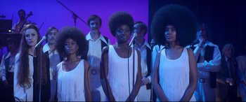 Movie still from “Elvis” (2022), directed by Baz Luhrmann – A group of people with afro hair sing together; Medium shot, Low angle