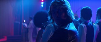 Movie still from “Elvis” (2022), directed by Baz Luhrmann – A man with long blonde hair is holding a microphone in front of a crowd; Close Up shot, Over the shoulder angle