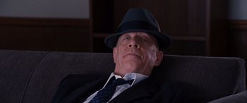 Movie still from “The Accountant” (2016), directed by Gavin O'Connor – A man in a suit and a hat sitting in a chair; Close Up shot, Low angle