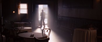 Movie still from “The Accountant” (2016), directed by Gavin O'Connor – A man standing in a doorway in a room with a chair; Wide shot, Low angle