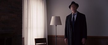 Movie still from “The Accountant” (2016), directed by Gavin O'Connor – An older man in a suit and hat standing in front of a lamp; Medium shot, Low angle