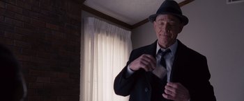Movie still from “The Accountant” (2016), directed by Gavin O'Connor – An older man wearing a suit and hat is putting on a tie; Medium shot, Low angle