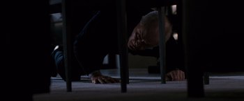 Movie still from “The Accountant” (2016), directed by Gavin O'Connor – An older man leaning on a chair under a table; Wide shot, High angle