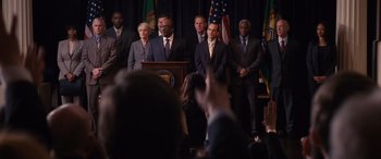 Movie still from “The Accountant” (2016), directed by Gavin O'Connor – A group of men and women standing in front of a podium; Medium shot, Low angle
