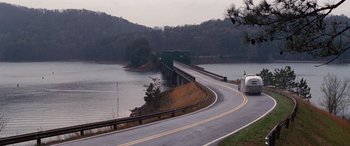 Movie still from “The Accountant” (2016), directed by Gavin O'Connor – A road going over a bridge near a body of water; Extreme Wide shot, High angle