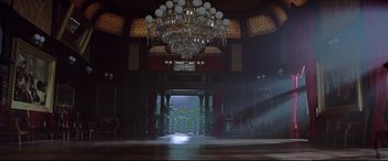 Movie still from “The Age of Innocence” (1993), directed by Martin Scorsese – A chandelier hangs in a large room with a light shining through; Extreme Wide shot, Low angle