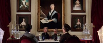 Movie still from “The Age of Innocence” (1993), directed by Martin Scorsese – A group of people sitting at a table in front of a painting of an older woman; Wide shot, Over the shoulder angle