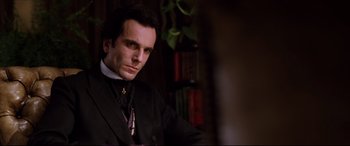 Movie still from “The Age of Innocence” (1993), directed by Martin Scorsese – A man wearing a suit and tie in front of a book shelf; Close Up shot, Low angle