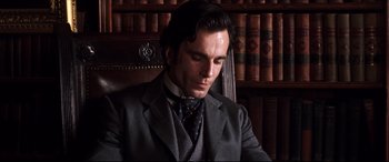 Movie still from “The Age of Innocence” (1993), directed by Martin Scorsese – A man in a suit and tie sitting in a chair; Close Up shot, High angle