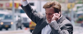 Movie still from “The Big Short” (2015), directed by Adam McKay – A man in a suit is holding his hand up in the air; Close Up shot, Low angle