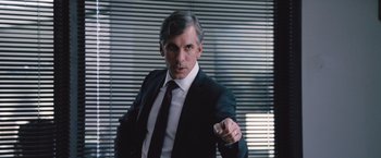Movie still from “The Big Short” (2015), directed by Adam McKay – A man wearing a suit and tie in front of a window; Medium shot, Over the shoulder angle