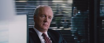 Movie still from “The Big Short” (2015), directed by Adam McKay – An older man wearing a suit and tie in front of a window; Close Up shot, Over the shoulder angle