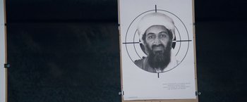 Movie still from “The Big Short” (2015), directed by Adam McKay – A picture of osama bin laden with a target in the background; Extreme Close Up shot, Overhead angle
