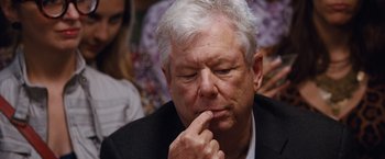 Movie still from “The Big Short” (2015), directed by Adam McKay – An older man with white hair is sitting in a crowd; Close Up shot, Over the shoulder angle