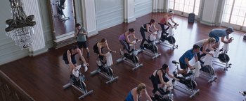 Movie still from “The Big Short” (2015), directed by Adam McKay – A group of people riding stationary bikes in a room; Extreme Wide shot, High angle