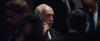 Movie still from “The Big Short” (2015), directed by Adam McKay – An older man in a suit and tie talking on a cell phone; Close Up shot, Over the shoulder angle