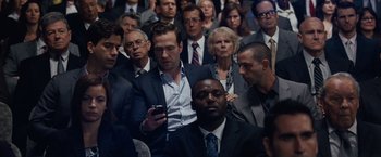 Movie still from “The Big Short” (2015), directed by Adam McKay – A crowd of people in suits and ties looking at a cell phone; Medium shot, Over the shoulder angle
