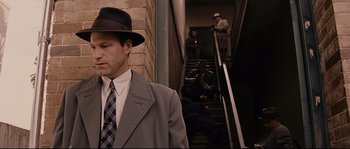 Movie still from “The Black Dahlia” (2006), directed by Brian De Palma – A man wearing a suit and a hat standing in front of a staircase; Medium shot, Over the shoulder angle