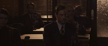 Movie still from “The Black Dahlia” (2006), directed by Brian De Palma – A man in a suit sitting in front of other men; Medium shot, Over the shoulder angle