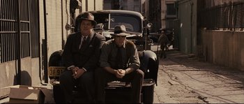 Movie still from “The Black Dahlia” (2006), directed by Brian De Palma – A couple of men sitting next to each other on the side of the road; Medium shot, High angle