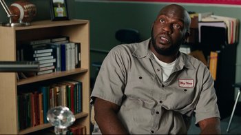 Movie still from “The Blind Side” (2009), directed by John Lee Hancock – A man sitting in front of a book shelf; Medium shot, Low angle